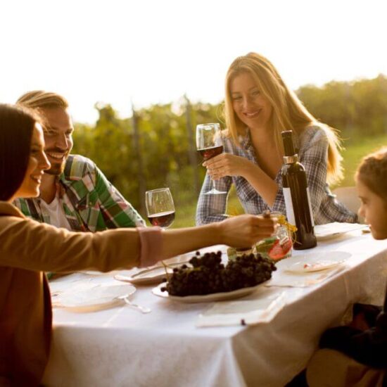 Famiglia seduti a tavola in campagna facendo una degustazione di vino