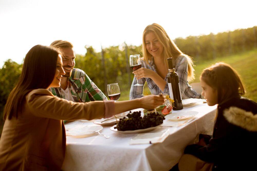 Famiglia seduti a tavola in campagna facendo una degustazione di vino