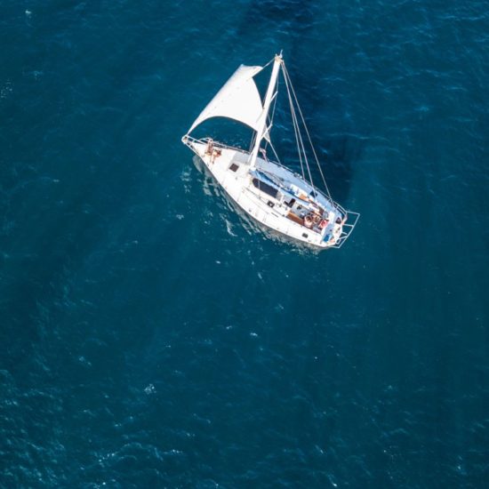 lonely isolated yacht under the sail with tall mast going in still sea aerial top view