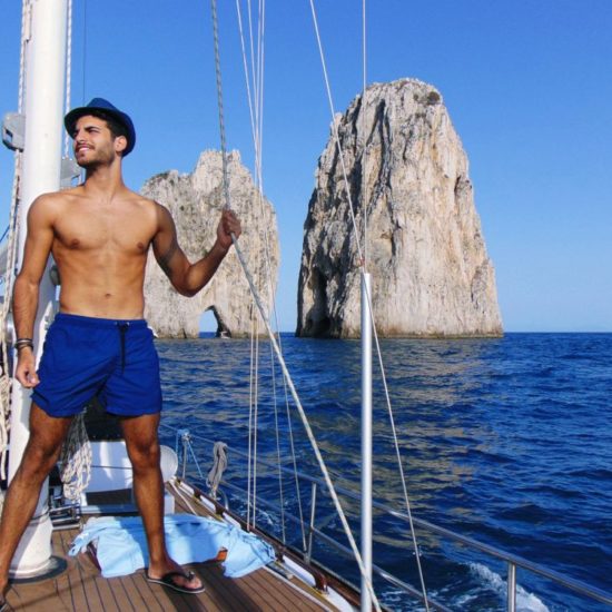 Young beautiful man standing in swimming suit on a yacht near blue sea water of Capri